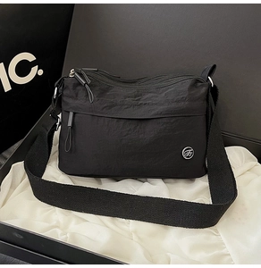 Detail of multi-compartment black nylon crossbody bag with waterproof texture and metal logo