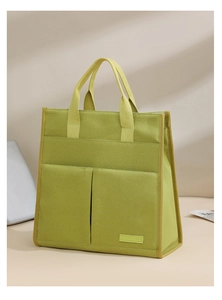 Detail of green canvas tote bag featuring dual front pockets and durable handles