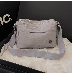 Detail of grey multi-compartment nylon crossbody bag with three zippers and metal logo