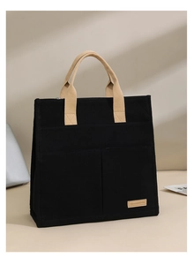 Detail of black canvas tote bag showing beige handles, outer pockets and textured fabric