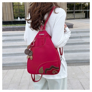 Detail of waterproof nylon backpack showing asymmetric zippers and decorative leaf pendant