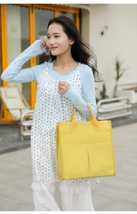 Detail of a bright yellow canvas tote bag featuring double front pockets and reinforced seams