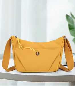 Vue détaillée du sac croissant en nylon jaune avec badge en métal et bandoulière tissée