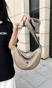 Dettaglio della borsa a mezzaluna in nylon beige con logo in metallo e tracolla