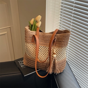 Dreifarbige Stroh-Tote-Bag mit braunen Lederriemen und dekorativer Quaste auf einem Stuhl