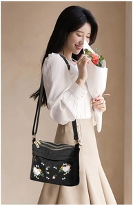 Detail of floral embroidery on black nylon shoulder bag with triple zip compartments