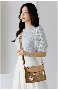 Detail of khaki nylon crossbody bag showing intricate floral embroidery and multi-zipper design