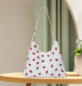 Detail of white strawberry print underarm bag with adjustable strap on wooden table