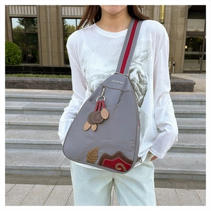 Detailed view of gray nylon crossbody bag with colorful leaf embroidery and leaf pendant
