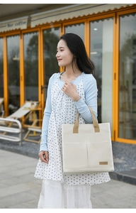 Detail of off-white canvas tote bag featuring double front pockets and brown handles