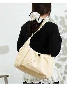 Detailed view of cream canvas tote bag with side drawstring pocket on model shoulder