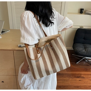 Detail of woven tote bag with vertical stripes, leather handles, and metal rivet reinforcement