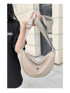 Dettaglio borsa a mezzaluna in nylon beige con tracolla larga e logo metallico