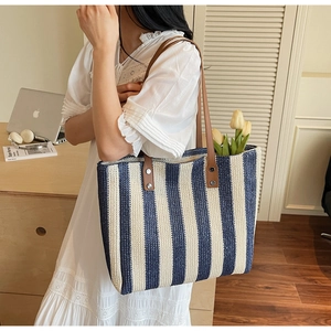 Detail of blue and white striped straw tote bag with brown leather handles and flowers