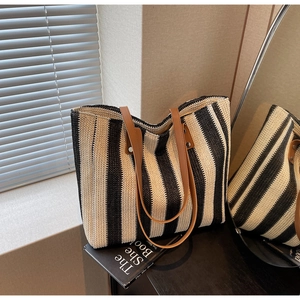Detail of hand-woven black and white straw tote bag with brown leather handles and rivets