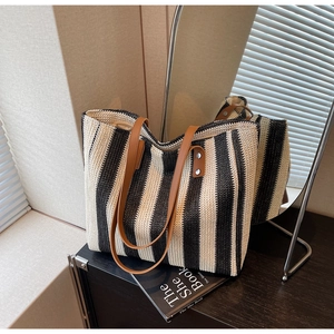 Detail of hand-woven straw tote with black and beige stripes and leather handles