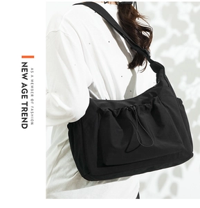 Detail of a black nylon tote bag with front drawstring pocket and wide shoulder strap