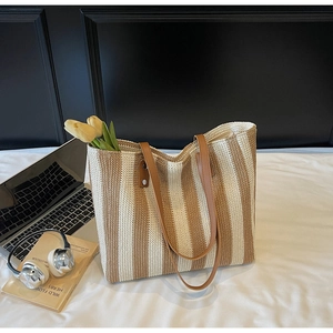 Detail of hand-woven straw tote bag with brown stripes and durable leather handles