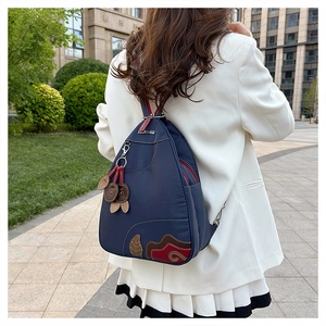 Detail of waterproof navy nylon backpack with leaf embroidery and decorative leather charms