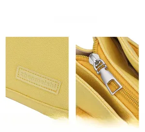 Detailed close-up of yellow canvas bag featuring rubber logo and smooth silver zipper