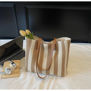 Detailed view of a striped woven tote bag with leather handles on a cozy bed background