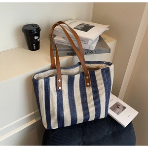 Detail of woven tote bag featuring navy stripes, brown leather handles and silver rivets