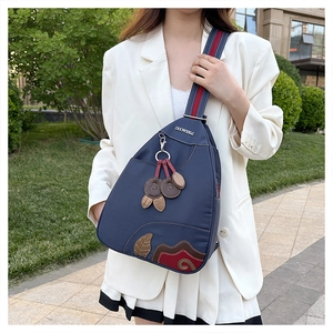 Detail of navy nylon chest bag with traditional embroidery and leaf charm pendant