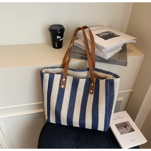 Detail view of blue and white striped straw tote bag with brown leather handles