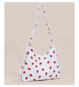 Detailed close-up of a white canvas shoulder bag featuring a vibrant red strawberry pattern