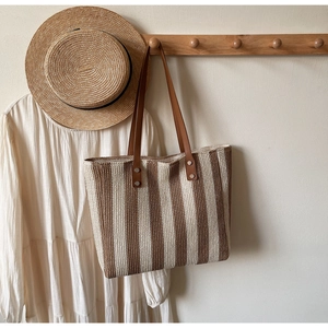 Detail of straw tote bag with brown leather handles and rivets on a white wall hook