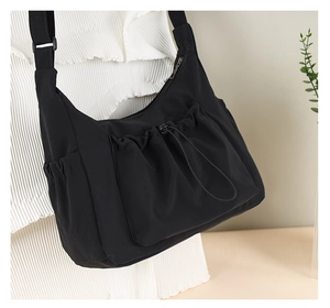 Detail of black crossbody bag showing drawstring front pocket and adjustable strap