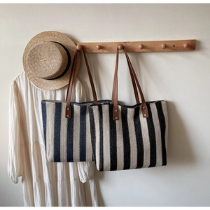 Detail of handwoven straw tote bag featuring leather straps and nautical stripes