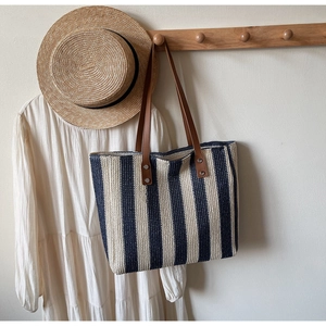 Detailed view of woven straw tote bag with navy stripes on a wooden clothes rack