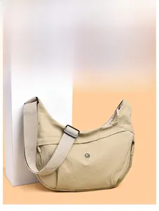 Detail of beige nylon crescent bag featuring adjustable black strap and round metal logo