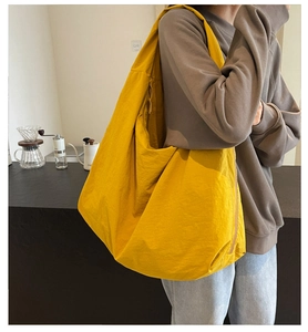 Bright yellow oversized nylon tote bag worn on shoulder in a cozy cafe setting