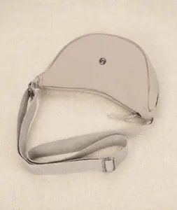 Dettaglio ravvicinato di una borsa a mezzaluna in nylon beige con tracolla regolabile e logo