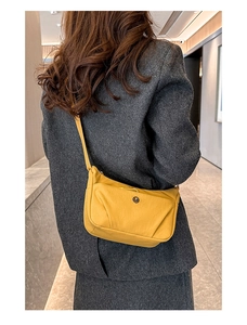 Détail d'un sac bandoulière en nylon jaune avec fermeture zippée et logo métallique discret