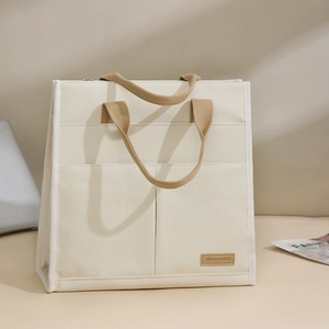 Minimalist cream canvas tote bag with brown woven handles and multi-pocket laptop storage