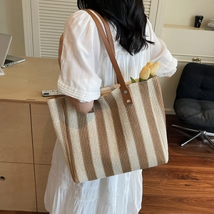 Handwoven straw tote bag with brown stripes and leather handles for vacation or beach