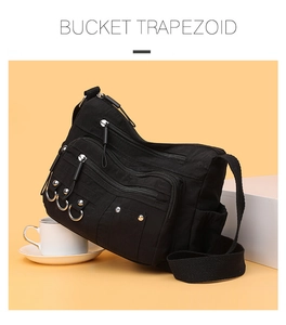Detail of black canvas crossbody bag with multiple silver rings and layered zipper pockets