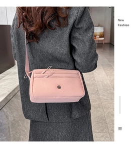 Detail der hellrosa Nylon-Umhängetasche mit rundem Metalllogo und breitem Gurt