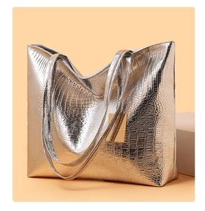 Detail van zilveren tote bag met krokodillenreliëf en een gouden metalen hanger accent