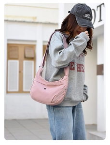 Pink nylon crescent crossbody bag featuring a wide strap and minimalist circular logo detail