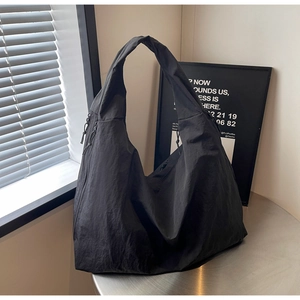 Close-up of a large black nylon tote bag with a relaxed hobo shape on a metal table