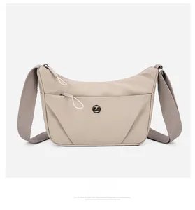 Détail du sac bandoulière en nylon beige avec deux zips frontaux et logo métallique rond
