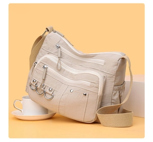 Detail of khaki nylon crossbody bag showing multi-pocket design and metal zippers