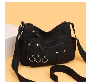 Detail of multi-pocket black nylon crossbody bag with silver metal rings and studs