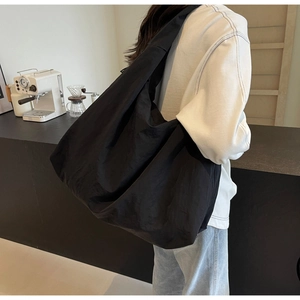 Detail of a large black nylon tote bag showing soft pleated texture on a shoulder strap