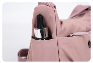 Détail de la poche latérale d'un sac à bandoulière en nylon rose avec flacon cosmétique