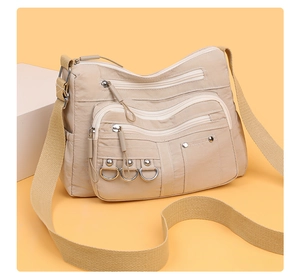 Close-up of beige nylon crossbody bag with multi-zipper pockets and metal D-ring detail